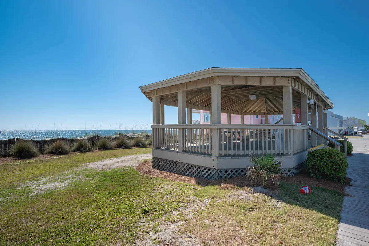 The image shows a gazebo on a landscaped grassy area overlooking the ocean. The open structure offers views of the water, ideal for outdoor gatherings, yoga, or quiet reflection.