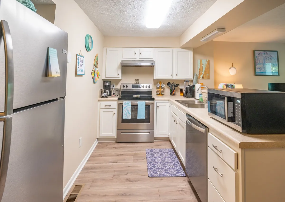 A stylish kitchen with stainless steel appliances, a central island, colorful wall art, and ample natural light streaming in. The scene is warm and functional, suggesting space for meal prep, entertaining, and gathering around the island.