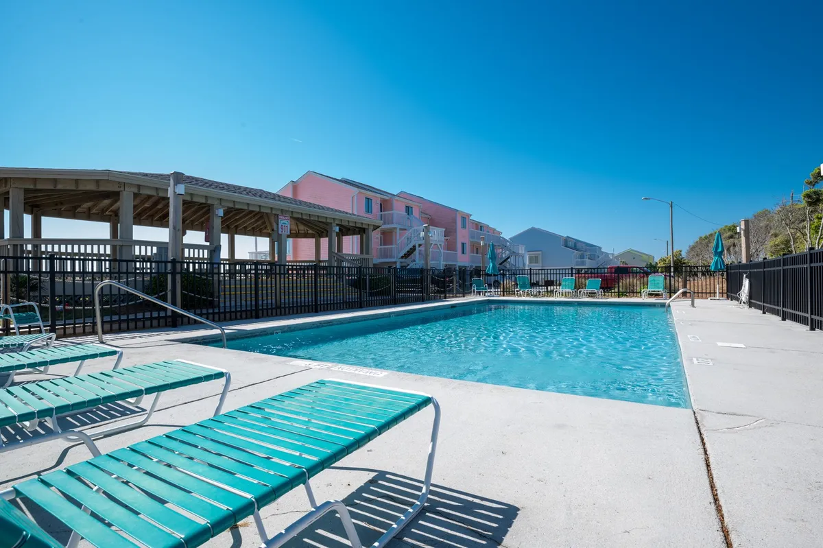 This exterior shot captures a sparkling swimming pool ringed by lounge chairs and bordered by neighboring buildings. The sun overhead and open layout evoke a mood of relaxation and leisure.