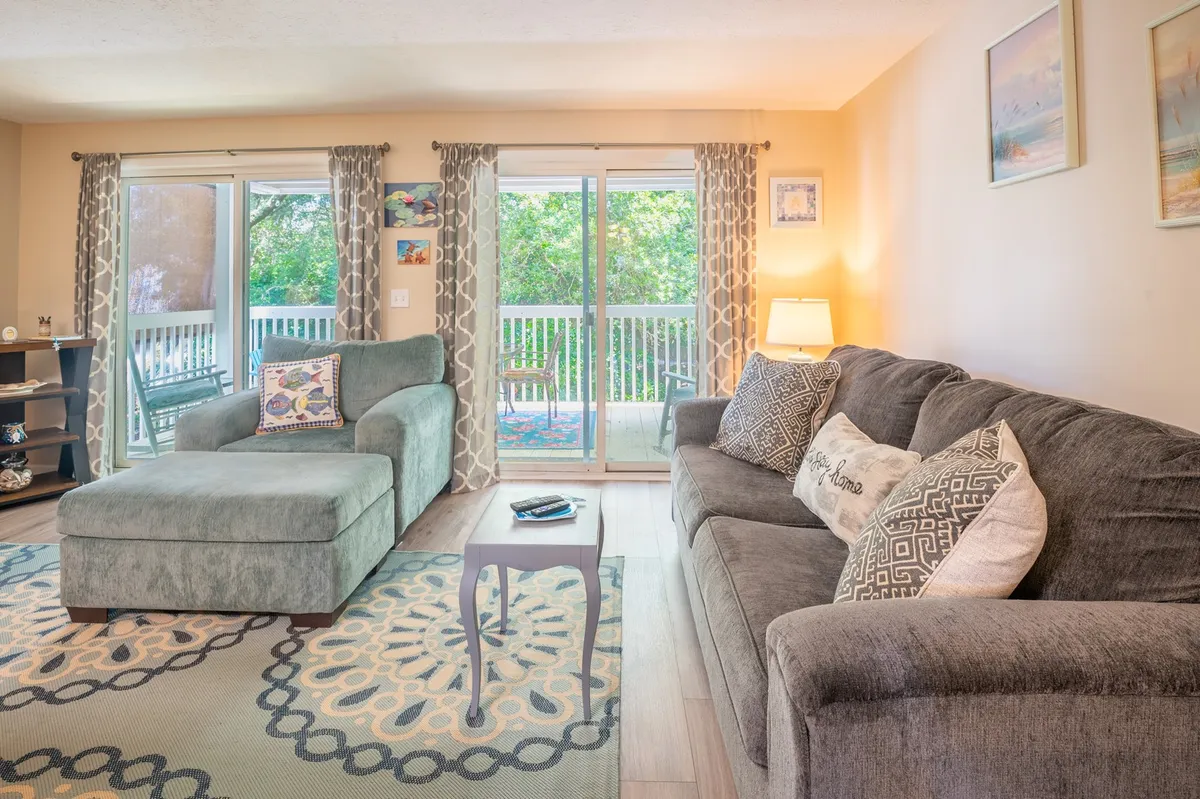 A cozy living room featuring a comfortable sofa, coffee table, decorative pillows, a stylish rug, and sliding glass doors that open to an outdoor space. The arrangement invites relaxation, conversation, and offers a glimpse of nature outside.