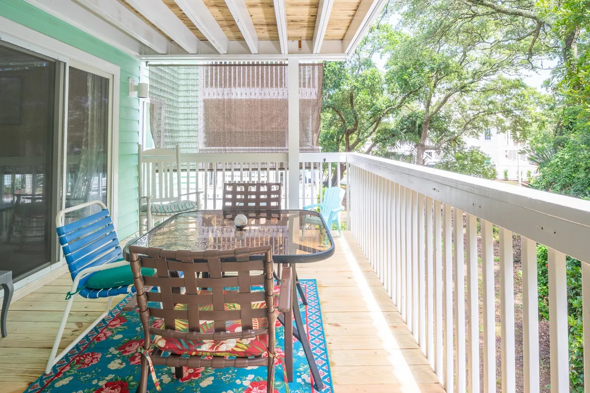 A cheerful covered porch with a glass table, colorful chairs, decorative rug, and a green wall, surrounded by greenery. The space is perfect for morning coffee, sunset cocktails, or relaxed outdoor dining.