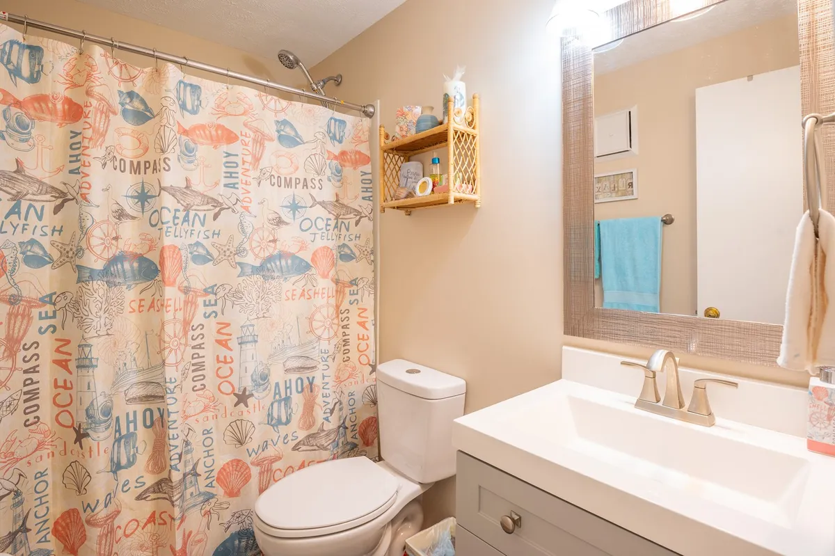 A bright, modern bathroom with a colorful shower curtain, contemporary vanity, and decorative shelving. Sunlight streams in through the window, creating a fresh and refreshing atmosphere ideal for self-care and unwinding after a long day.