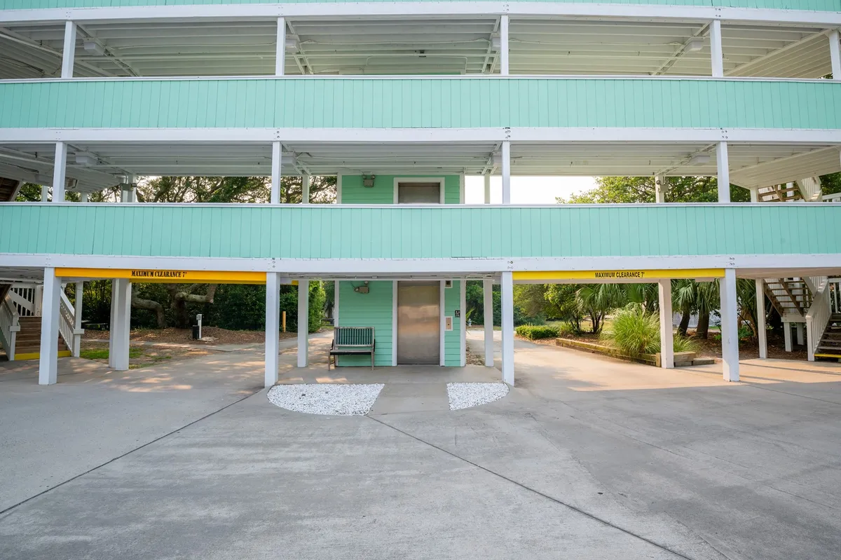 An exterior scene showing the elevator, a green bench for guests to relax on, white gravel ground, and palm trees. The area is casual and inviting, suggesting a spot to pause while waiting for the elevator or to enjoy the outdoors upon arrival.